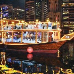 A traditional dhow boat lit up at night on the Marina with a view of Dubai's skyline in the background.