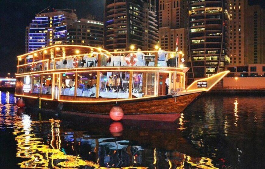 A traditional dhow boat lit up at night on the Marina with a view of Dubai's skyline in the background.
