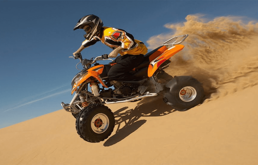A person riding a quad bike in the desert with sand dunes in the background.