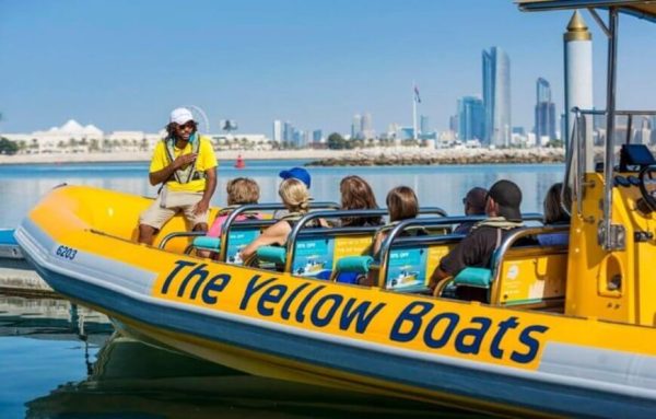 Yellow boat sailing through Dubai Marina with skyscrapers in the background.