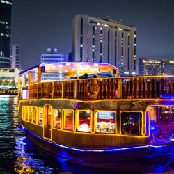 A traditional dhow boat lit up with colorful lights and decorations, sailing down the Dubai Water Canal with the city's modern skyline in the background