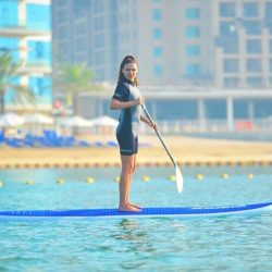 Person standing on a paddleboard in the calm waters of Dubai, with the city skyline in the background